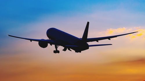 Low angle view of airplane flying in sky during sunset