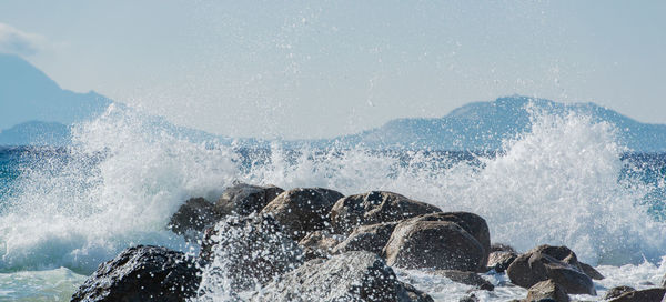 Sea waves splashing on rocks against sky