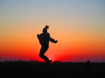 Silhouette man jumping against orange sky