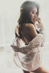 Side view of young woman standing against window