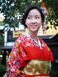 Portrait of smiling young woman standing against tree