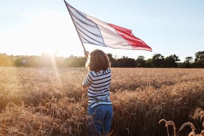 Rear view of boy standing with french flag on field against sky