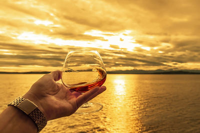 Swirling a alcoholic drink in a crystal snifter glass during golden sunset over the sea.