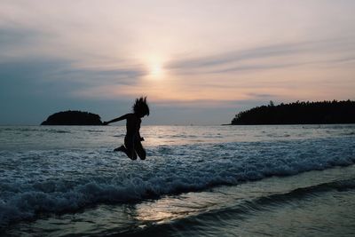 Woman jumping over sea against sky during sunset