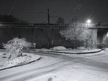 Snow covered railroad tracks by road against sky at night