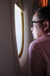 Side view of mature man looking through window while sitting in airplane