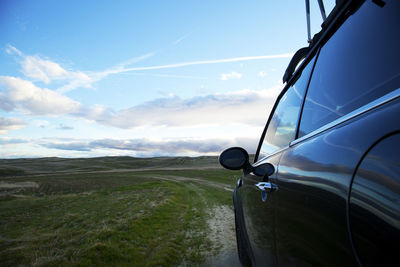 Sports car on dirt road in field with clouds in sky