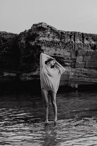 Rear view of woman standing on rock in sea against sky