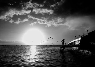 Silhouette man standing by sea against sky during sunset