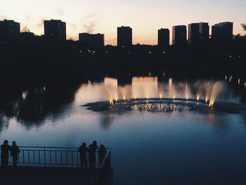 Silhouette people on riverbank against sky in city