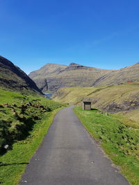 Road leading towards mountains against clear blue sky