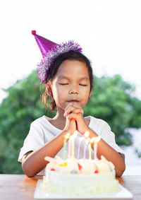 Birthday girl wishing while wearing party hat at home