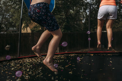 Low section of sisters jumping on trampoline against trees at park