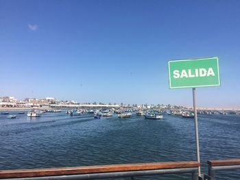 Information sign by sea against clear blue sky