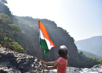 Rear view of woman standing on mountain against sky with indian flag