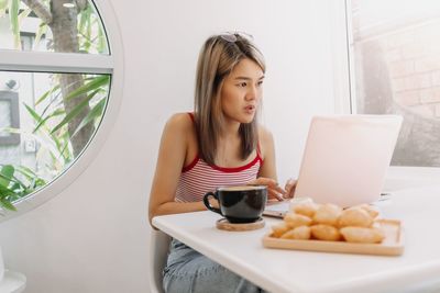 Young woman using laptop while sitting on table