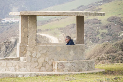Rear view of woman sitting on retaining wall against sky