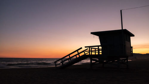 Silhouette lifeguard hut on beach against clear sky during sunset