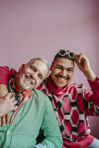 Portrait of gay friends with arm around against pink wall at home