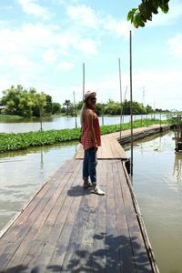 Woman standing on pier over lake against sky