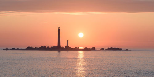 Silhouette lighthouse by sea against sky during sunset