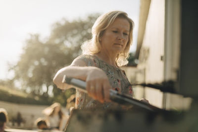 Mature woman preparing food on barbecue grill during dinner party