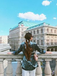 Woman standing by fountain in city against sky