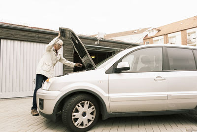 Senior woman opening car hood while standing by warehouse