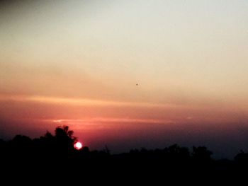 Silhouette trees against orange sky