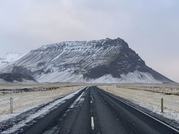 Road leading towards snowcapped mountains against sky