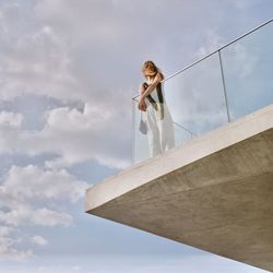 Low angle view of young woman standing in balcony against sky