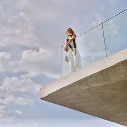 Low angle view of young woman standing in balcony against sky