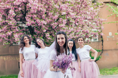 Portrait of smiling young woman standing by pink flowering plants