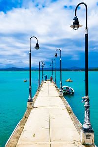 Street lights on pier by sea against sky