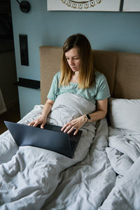 Young woman using phone while lying on bed at home