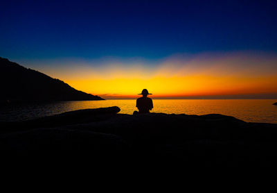 Silhouette man looking at sea against sky during sunset