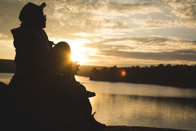 Silhouette woman sitting by lake against sky during sunset