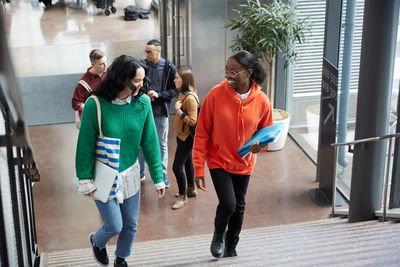 High angle view of female friends walking on steps against friends standing in university