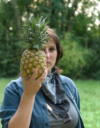 Portrait of woman holding fruit against tree