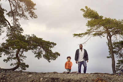 Father and son walking amidst trees against sky