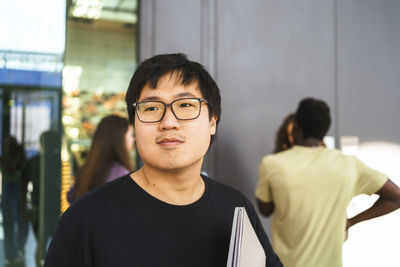 Young male student wearing eyeglasses looking away in college campus