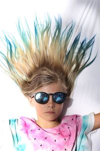 Directly above shot of girl with dyed hair wearing sunglasses lying on bed at home