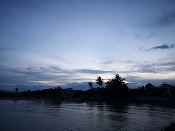 Silhouette trees by lake against sky at sunset