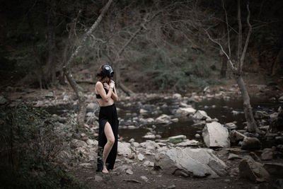 Side view of woman wearing gas mask while covering chest in forest