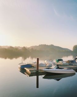 Boats moored in lake against sky during sunset