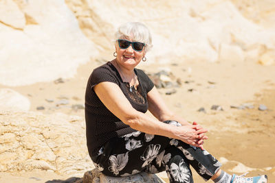 Old woman in black clothes sitting on a rock near the sea