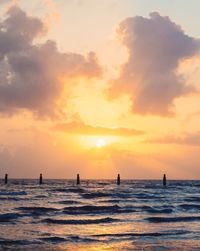 Silhouette wooden posts in sea against cloudy sky during sunset