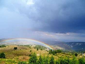 Scenic view of double rainbow on landscape against cloudy sky
