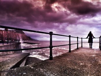 People standing on bridge against cloudy sky