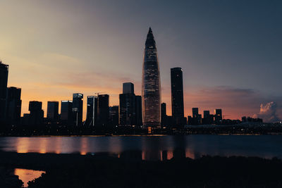 Sea by modern buildings against sky during sunset